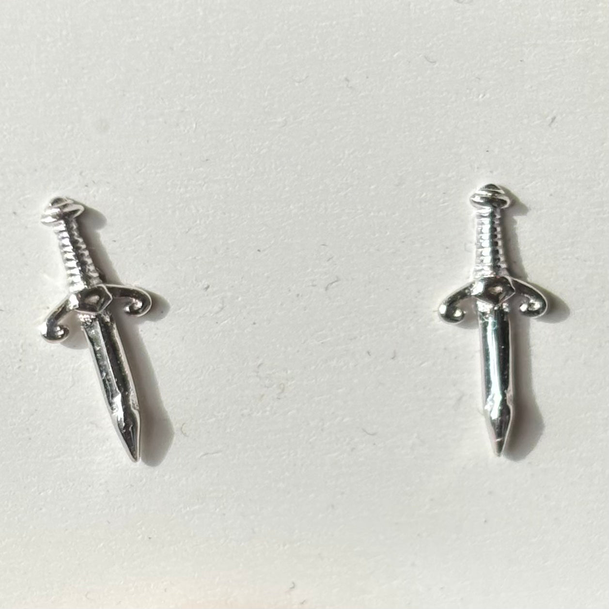 Silver sword-shaped earrings on a light gray background