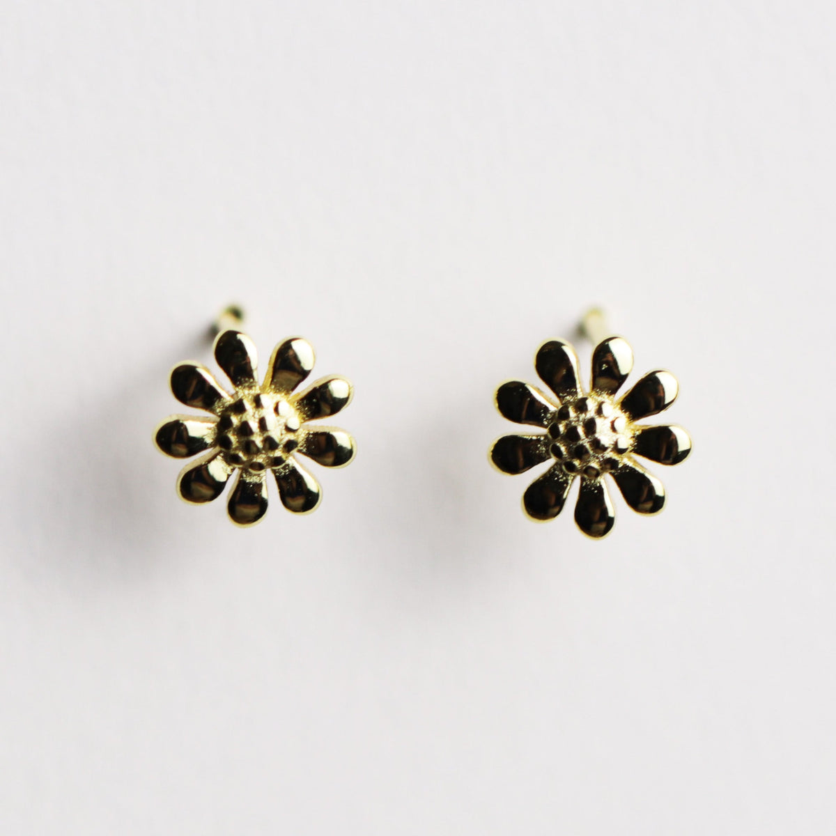 A pair of gold flower stud earrings with textured centers and small darkened petal accents, shown on a plain light background.