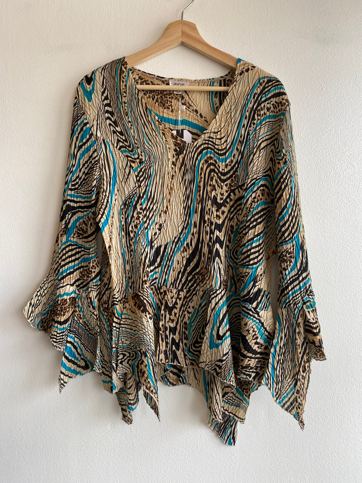 A long-sleeve V-neck top with an abstract wavy pattern in beige, black, and turquoise blue, hanging on a wooden hanger against a white wall.
