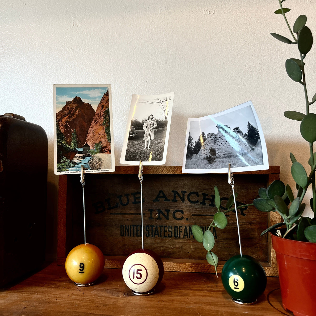 Three pool ball photo holders with numbers attached to them, each holding a small photograph, on a wooden surface.