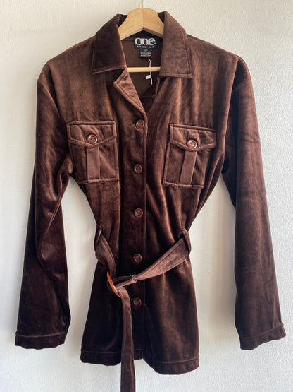 A dark brown velvet long-sleeve shirt jacket with a matching tie belt, hanging on a wooden hanger against a white wall. The brand label 'one step up' is visible inside the collar.