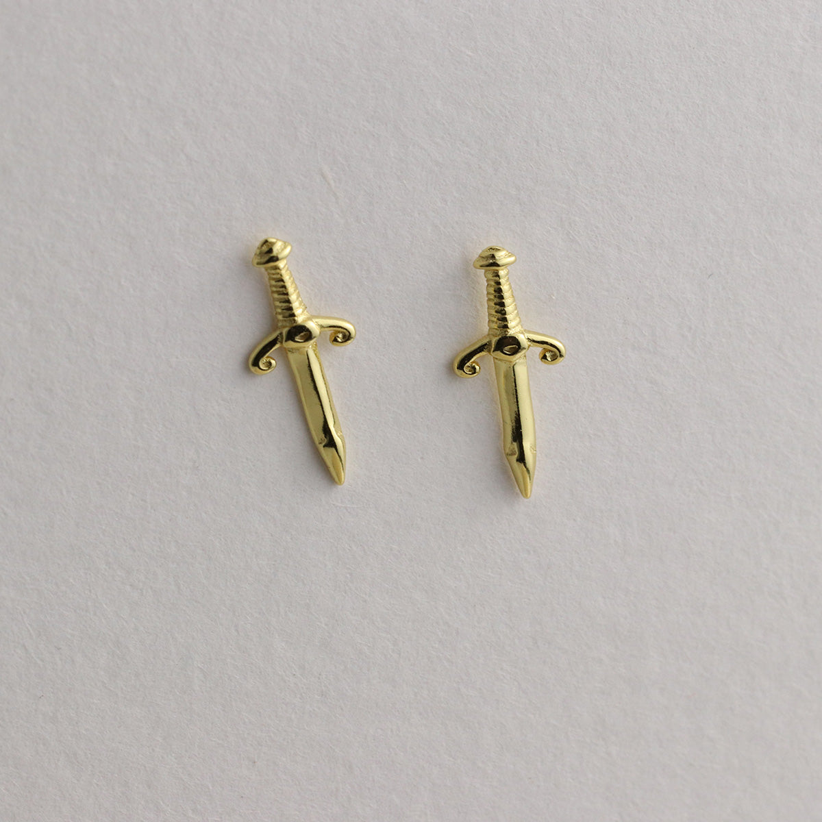 Gold sword-shaped earrings on a light gray background
