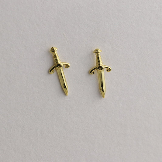Gold sword-shaped earrings on a light gray background