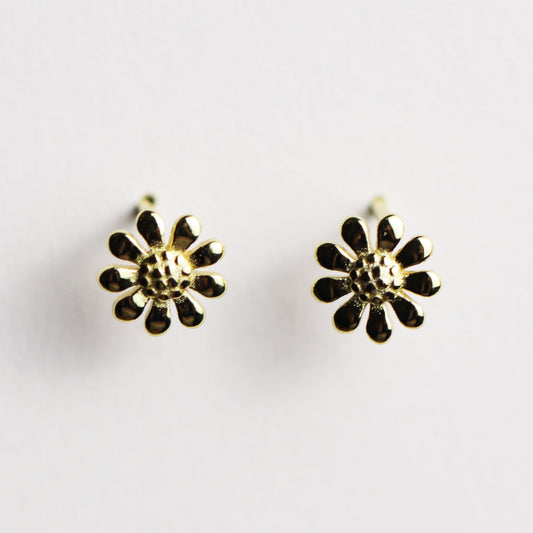 A pair of gold flower stud earrings with textured centers and small darkened petal accents, shown on a plain light background.